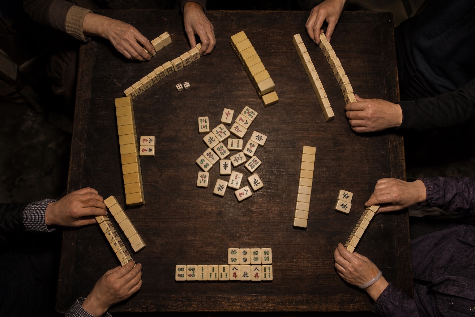 A mahjong table seen from above as four players arrange tiles.