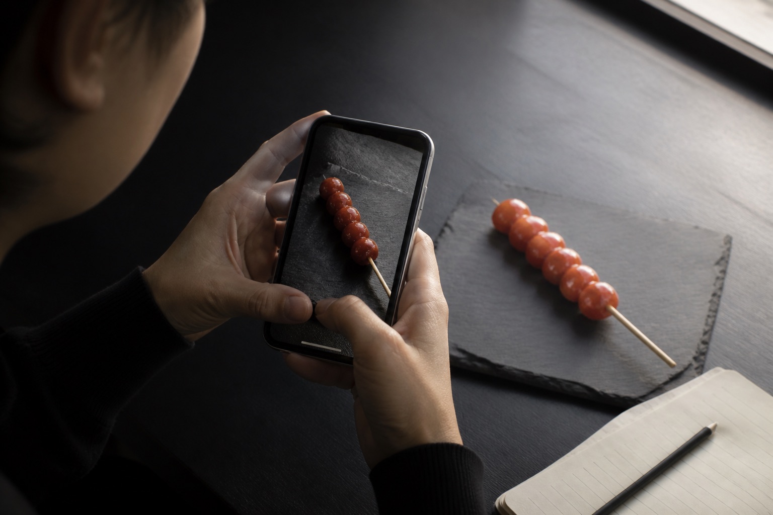 A researcher using a smartphone to photograph tanghulu on a dark surface.