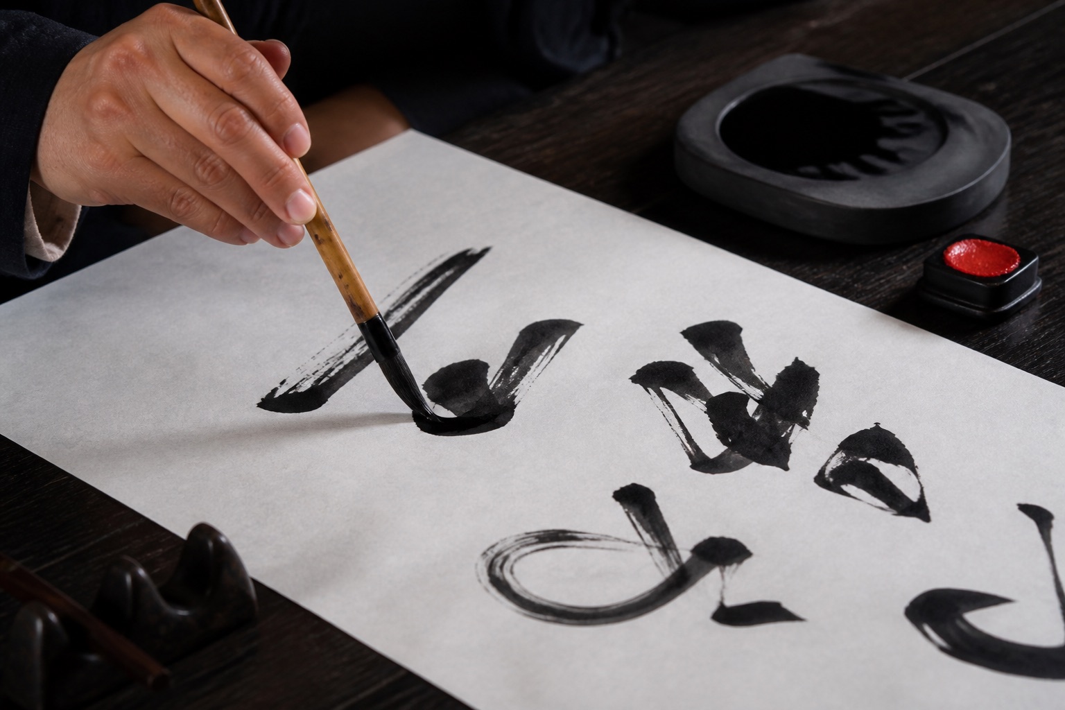 A calligrapher guiding an ink brush across white paper beside an inkstone.